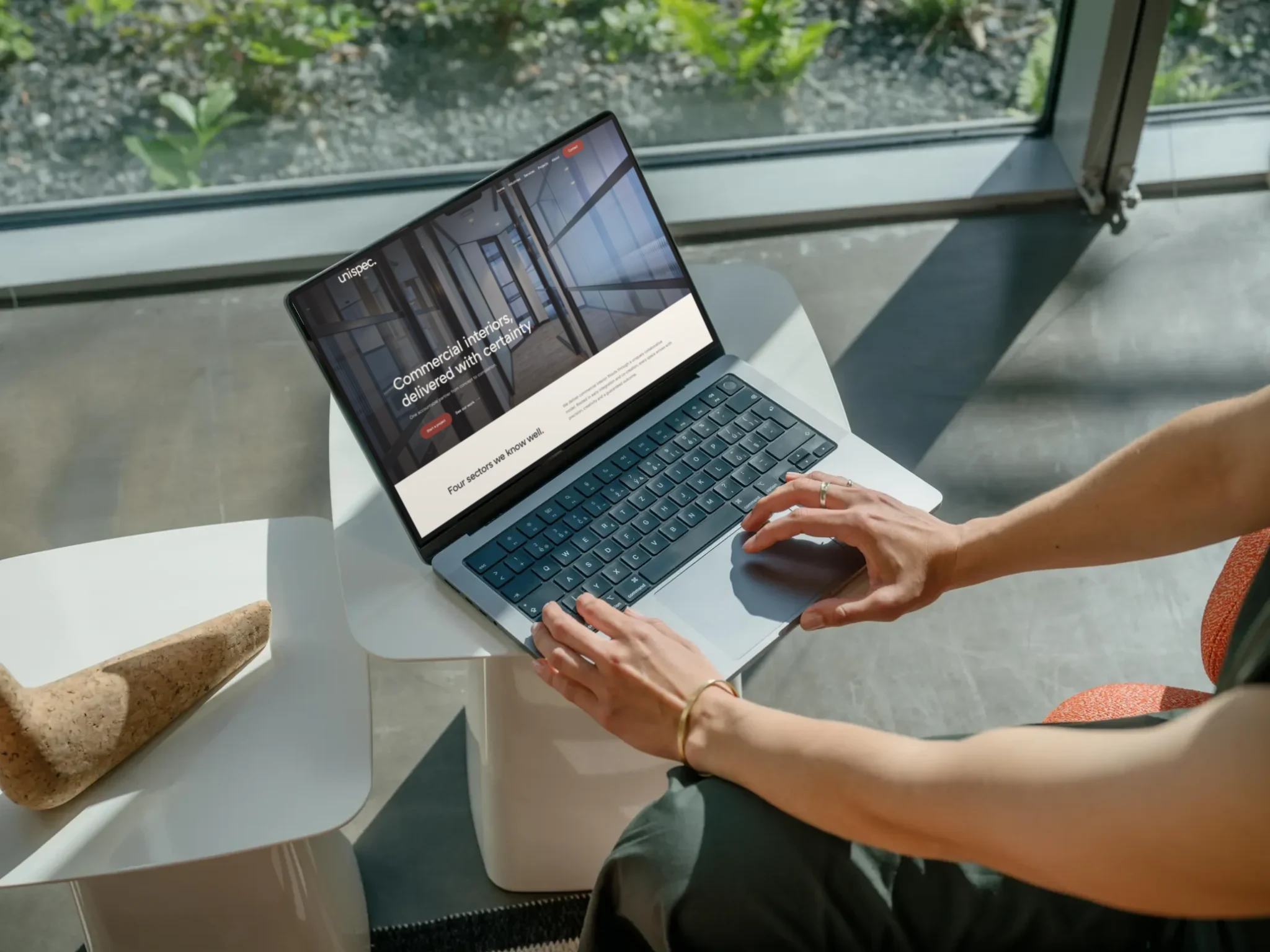 Unispec website homepage on a laptop in a sunlit office lounge