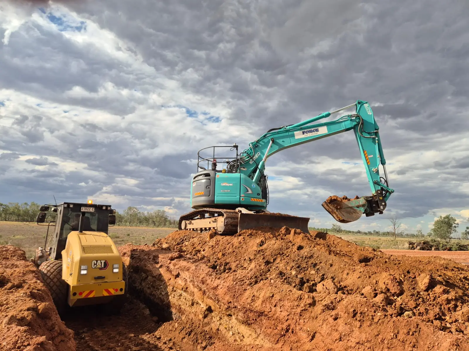 Force Civil excavator and roller building an embankment on a rural earthworks site