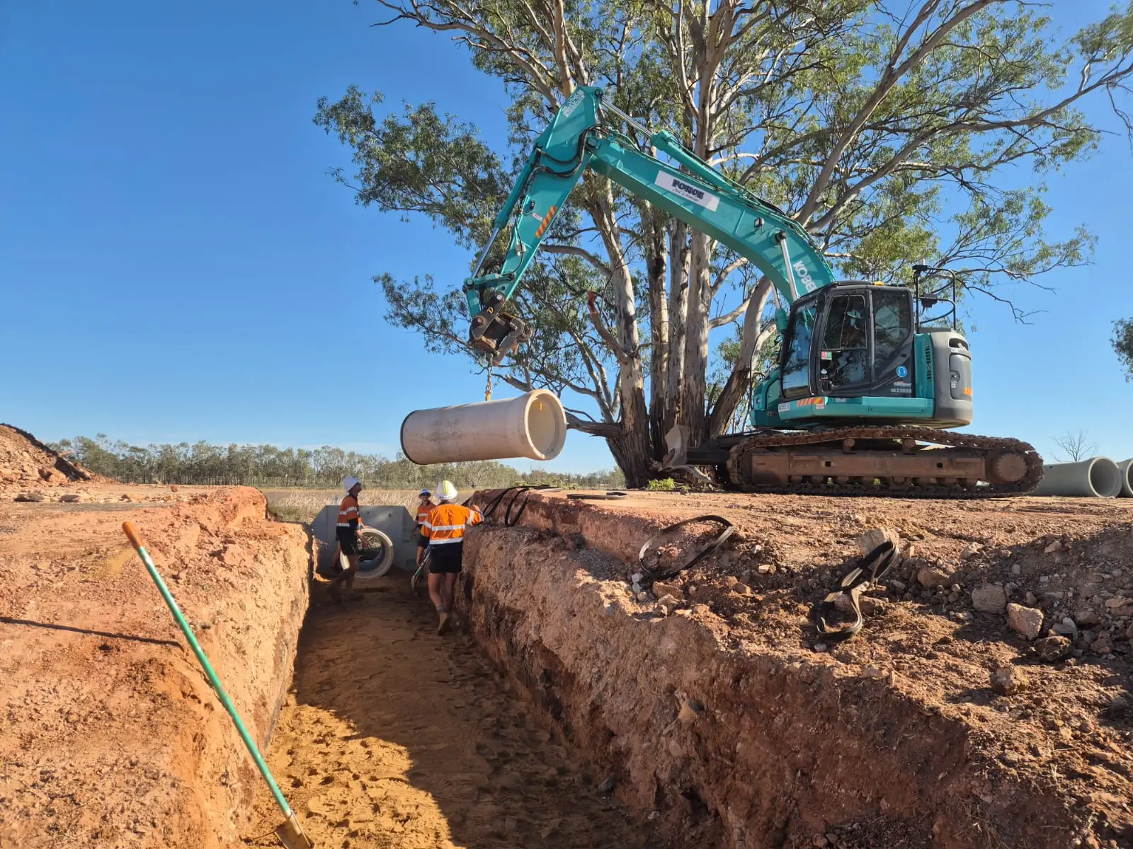 Force Civil excavator lowering a concrete drainage pipe into a trench